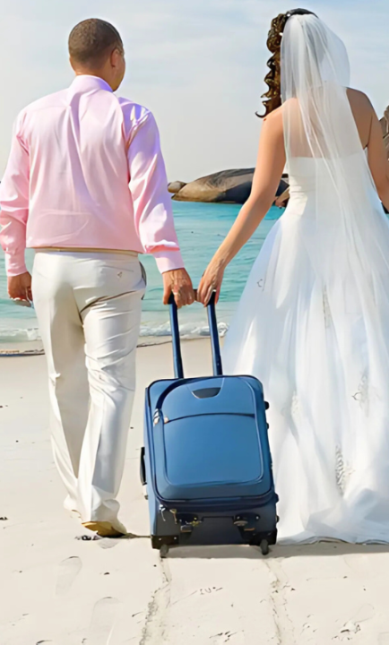 Paar in Anzug bzw. Brautkleid und kleinem Koffer laufen über Strand