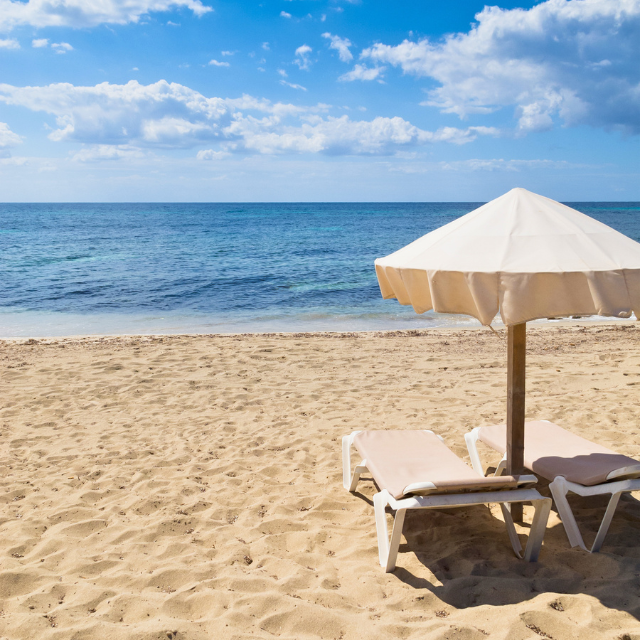Heller Sand mit einem Paar Liegen und einem Schirm im Vordergrund und dem Meer im Hintergrund