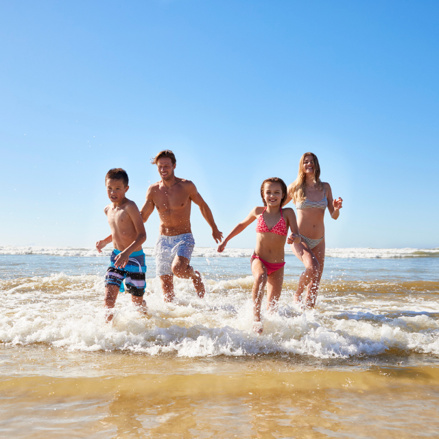 Eltern mit Sohn und Tochter rennen lachend durch Wellen am Strand