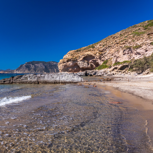 Klares Wasser auf eher kiesigem Untergrund mit Felsen im Hintergrund