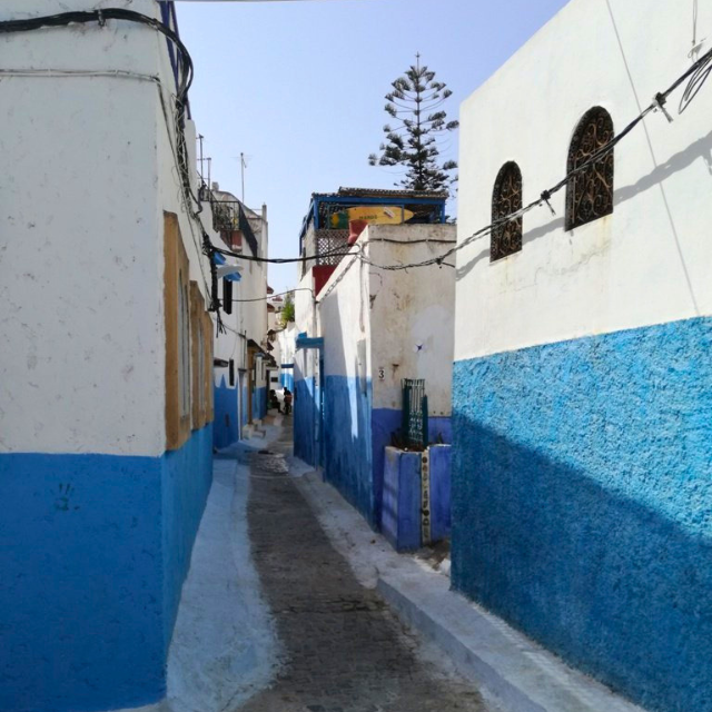 Enge Gasse mit zweifarbigen, verputzten Hausmauern: oben weiß, unten blau