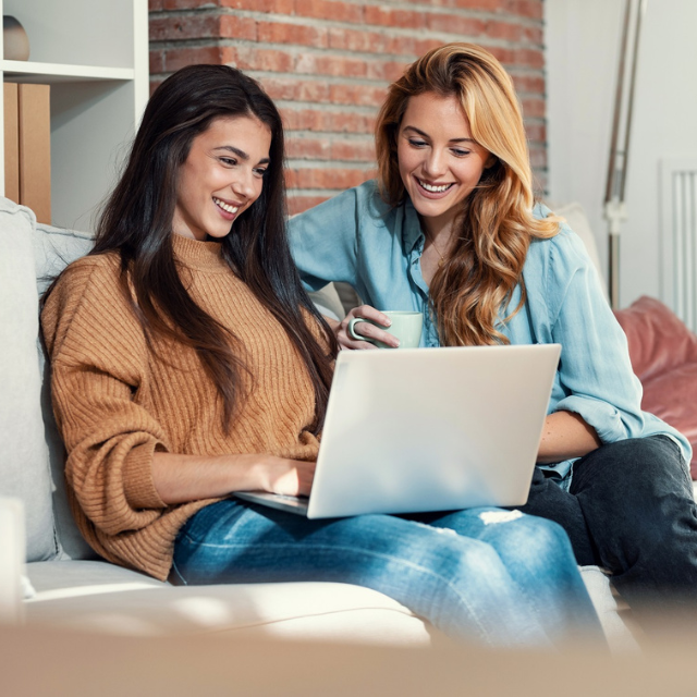 Zwei junge Frauen am Sofa mit Laptop