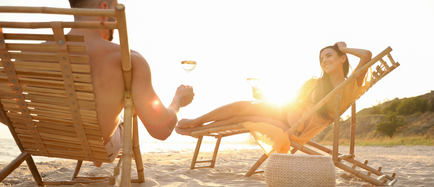 Paar mit Weingläsern am Strand bei Sonnenuntergang