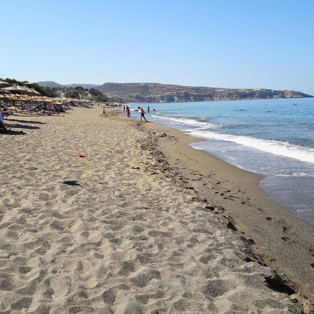 Blick entlang des weitläufigen Komos Beach mit einigen Liegen und Schirmen links