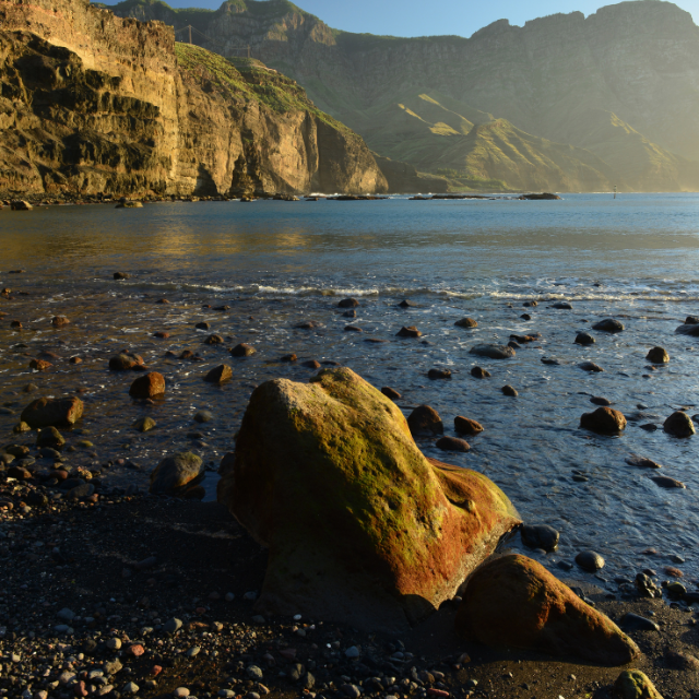 Felsiger Wasserzugang mit Klippen im Hintergrund bei Abendstimmung