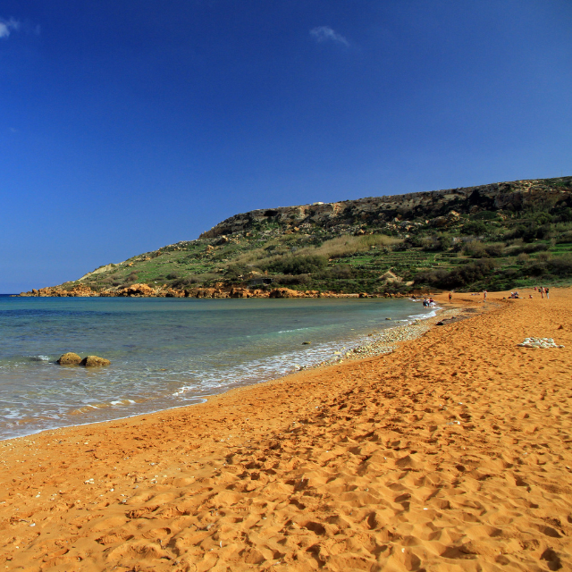 Rotgoldener Sand von Ramla Bay vor einer Klippe im Hintergrund