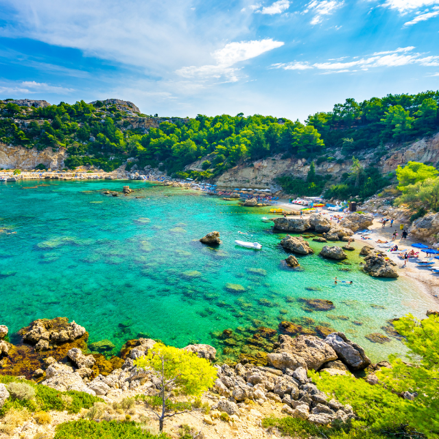 Blick auf das türkisgrüne Wasser der Bucht, umgeben von Felsen und Vegetation