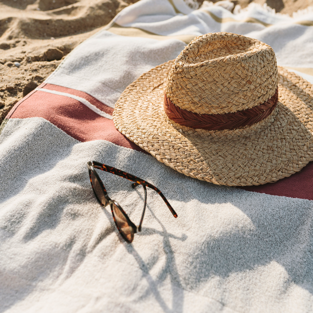 Handtuch auf Sand mit Strohhut und Sonnenbrille darauf