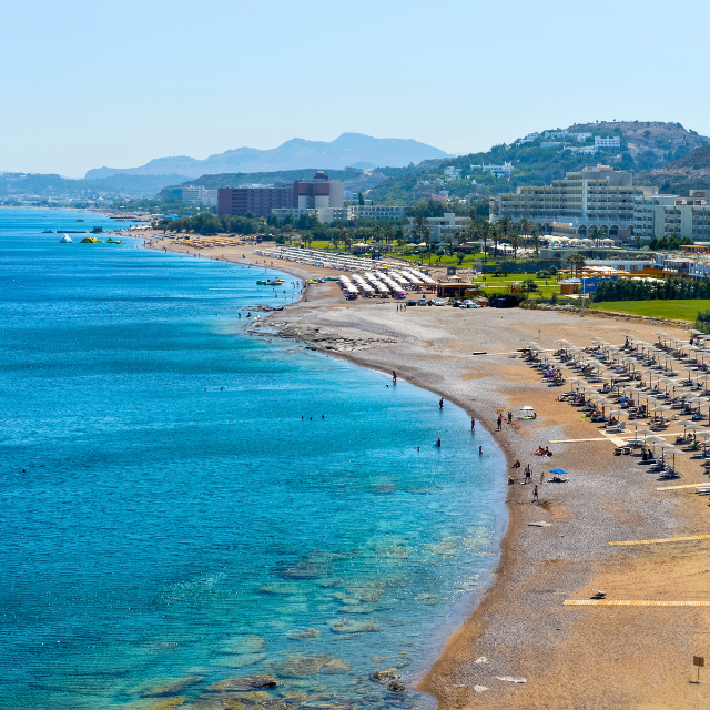 Blick entlang des Falikraki Beach mit Hotels und Bergen im Hintergrund