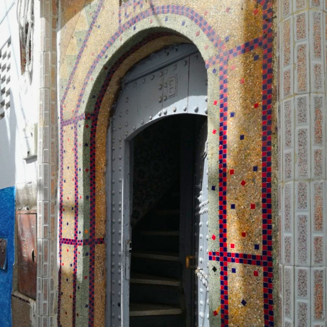 Mosaikgesäumte Tür mit Torbogen, geöffnet zu einem Innenraum mit Treppe