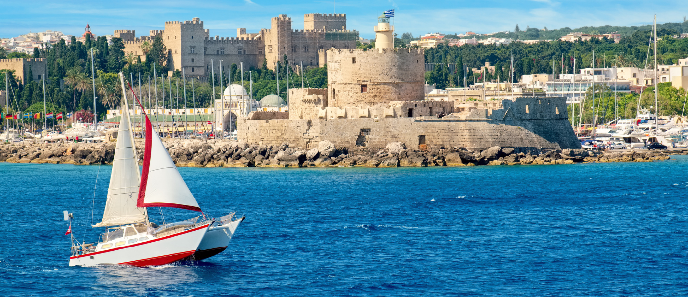 Blick in den Hafen auf die Mauern und Türme des Agios Nikolaos Kastell. Im Vordergrund ein Segelboot